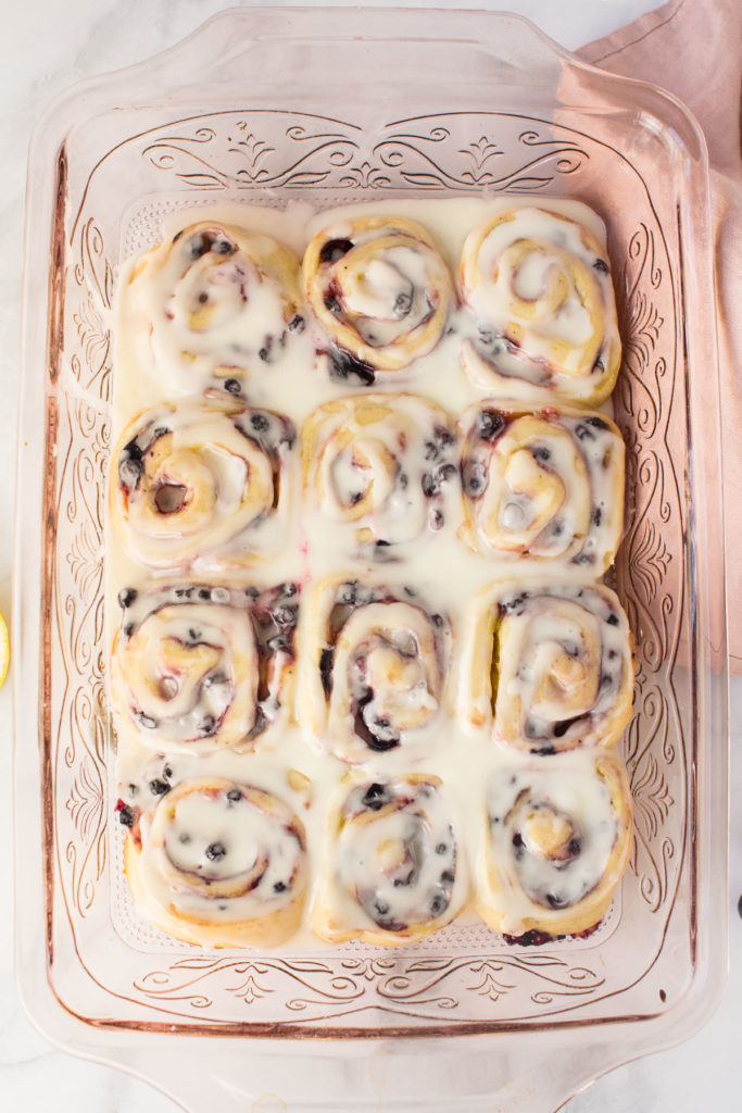 A pink pan holds 12 fruit sweet rolls topped with white icing. There is a pink napkin underneath the right side of it.