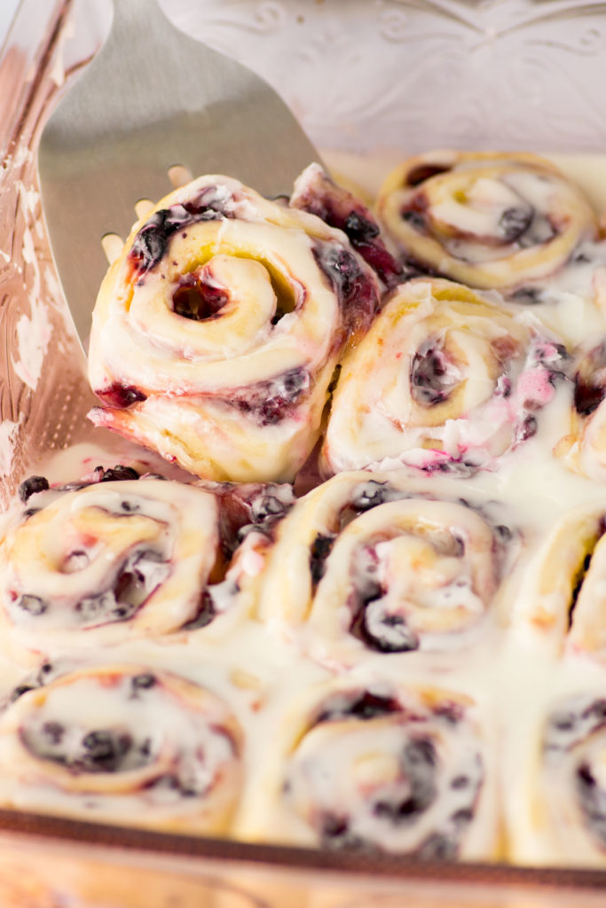 A pink pan has fruit sweet rolls topped with white icing.