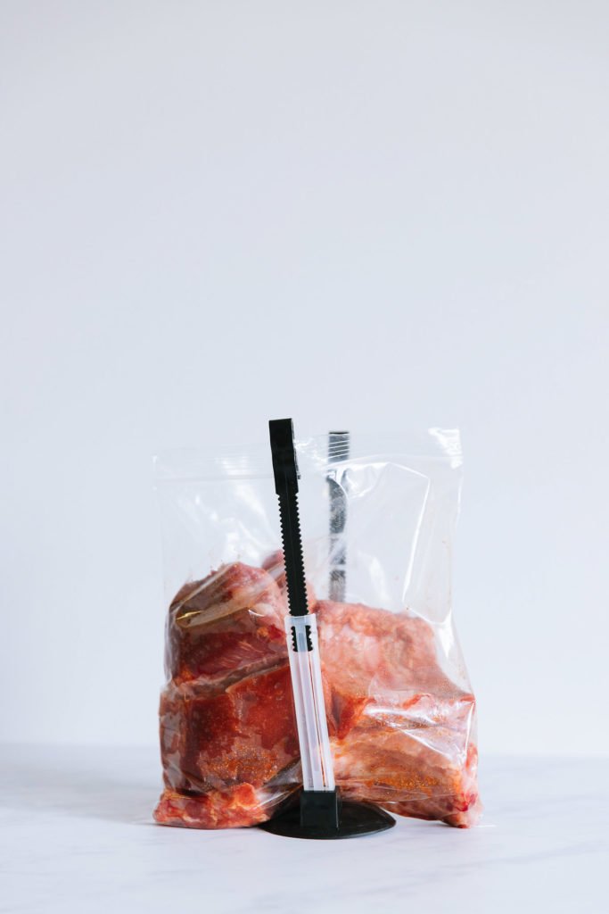 A gallon size ziploc bag filled with racks of uncooked ribs held open with freezer bag stands.