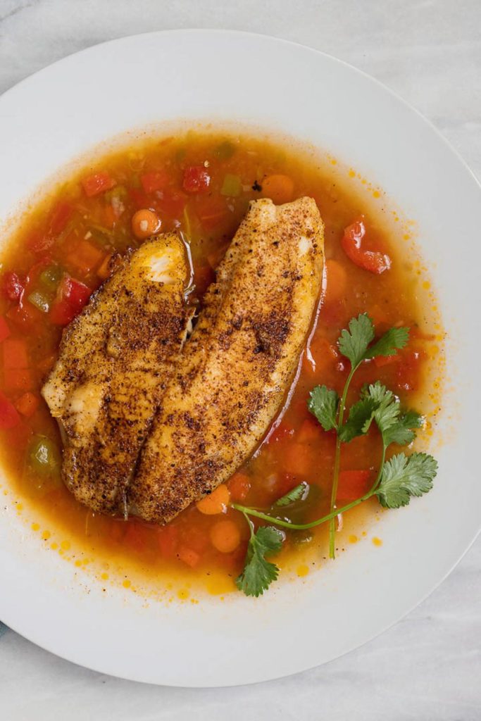 Overhead shot of Moqueca brazilian fish soup recipe with tilapia, carrots, tomatoes and cilantro in a white bowl. 