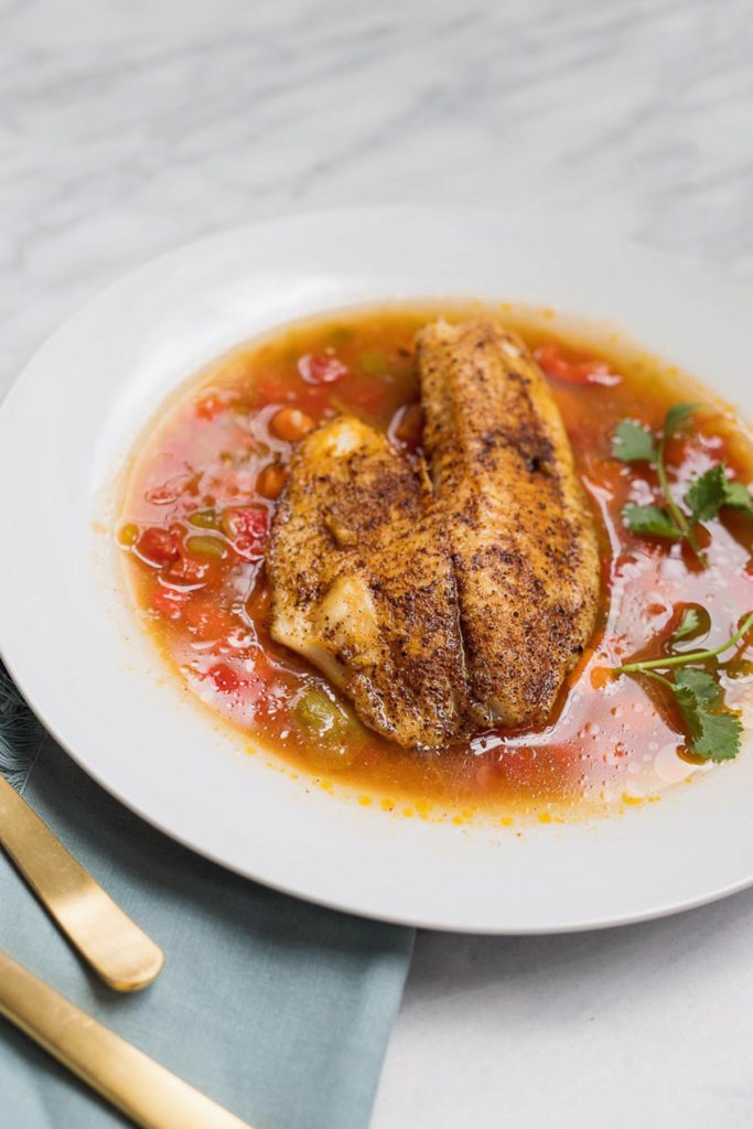 Tilapia pan seared and added to moqueca soup in a white bowl with cilantro.