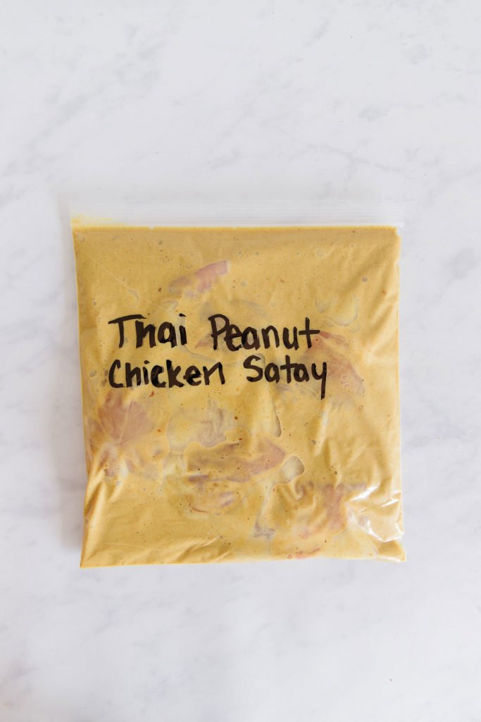 There is a gallon size zippered bag with raw chicken in a peanut chicken satay recipe inside of it.  The words "Thai Peanut Chicken Satay" are written in black marker on the bag.