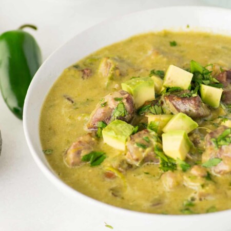 Bowl of pork chili verde topped with pieces of avocado.