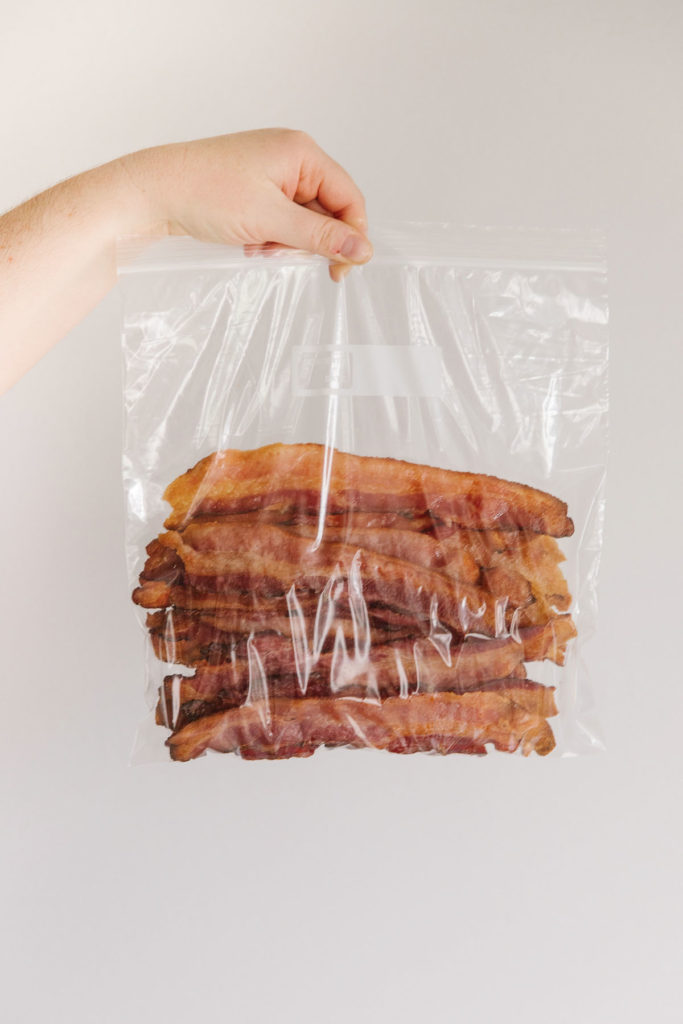 Strips of bacon in a zippered gallon-size bag with a hand holding it.