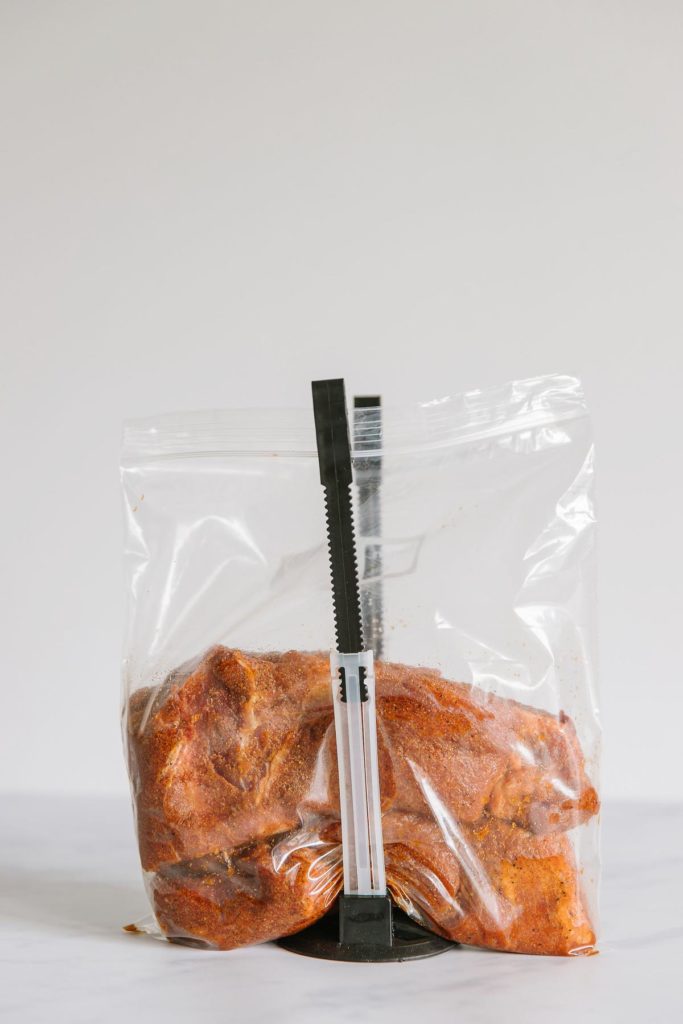 A gallon-size zippered freezer bag and holder holding it open with two pieces of seasoned pork in it ready to make my pulled pork sliders slow cooker recipe.
