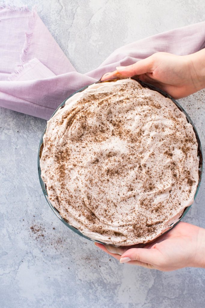 Two hands are holding a chocolate ice cream pie. There is a pink towel on the side.