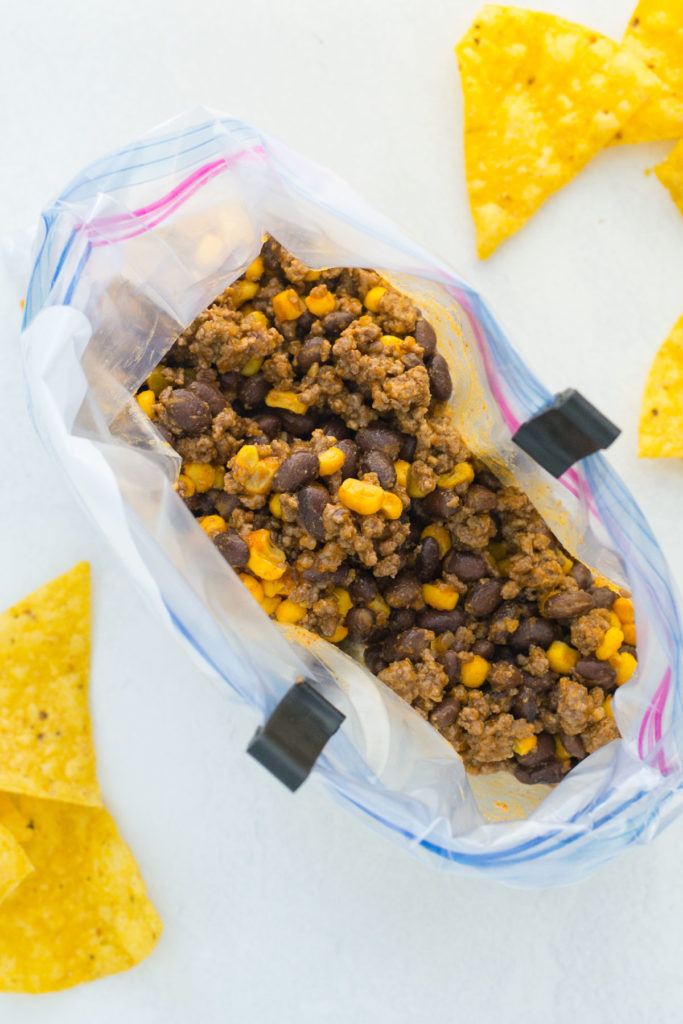 A zippered bag with a mixture of seasoned ground beef, beans and corn in it.  There are a few corn tortilla chips around it.
