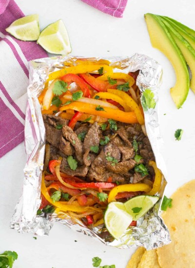 Steak fajita foil packed with peppers, limes, and avocado.
