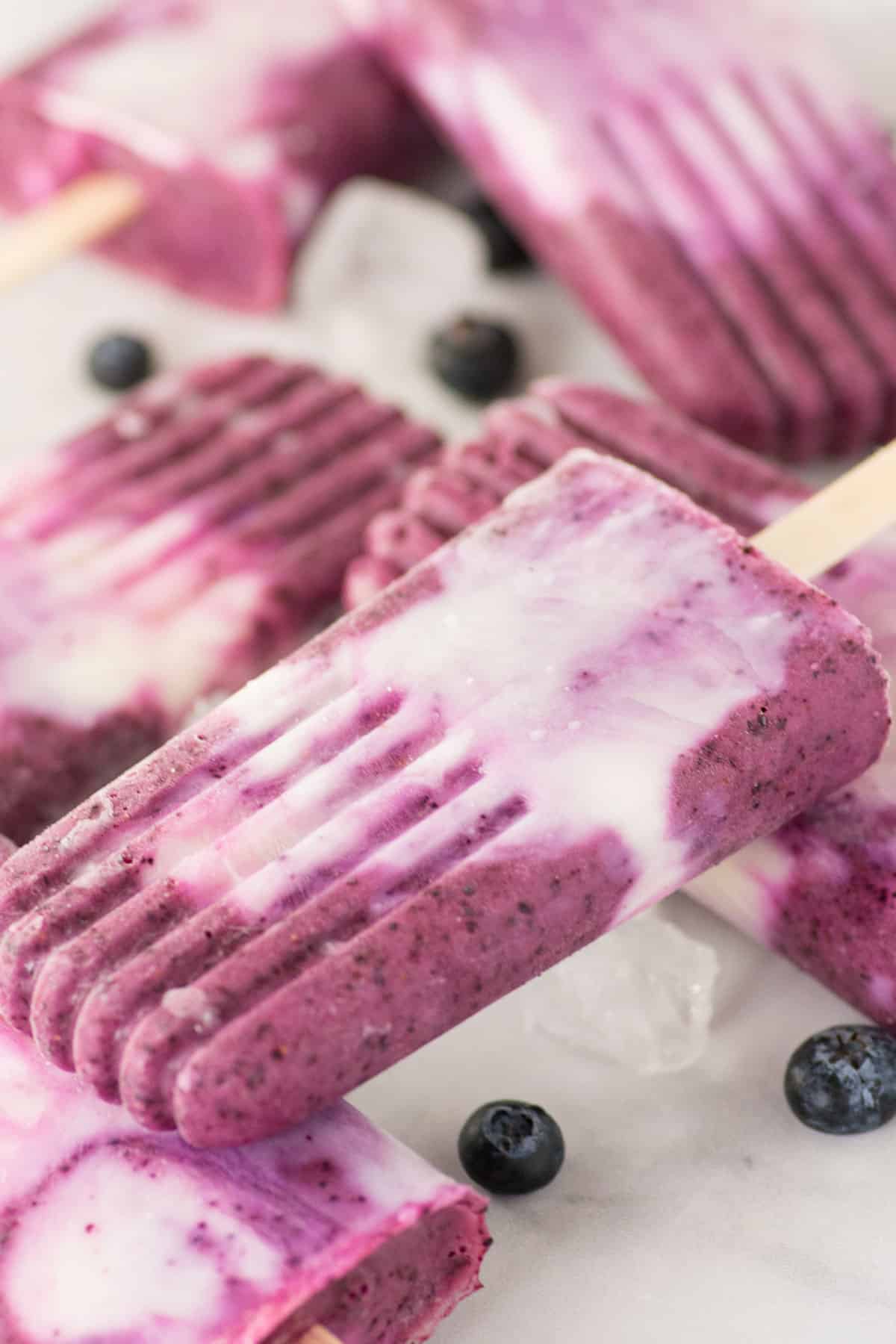 Blueberry Orange Homemade Popsicles stacked together with some blueberries scattered about.