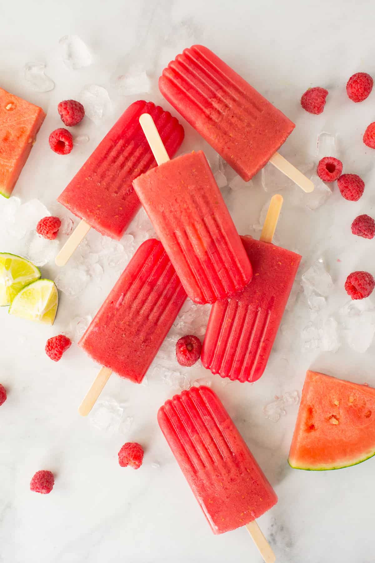 Raspberry Watermelon flavored homemade healthy popsicles on a white counter with raspberries and fresh watermelon