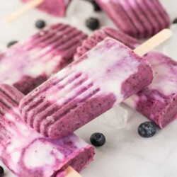 Purple and white popsicles on a countertop with blueberries.