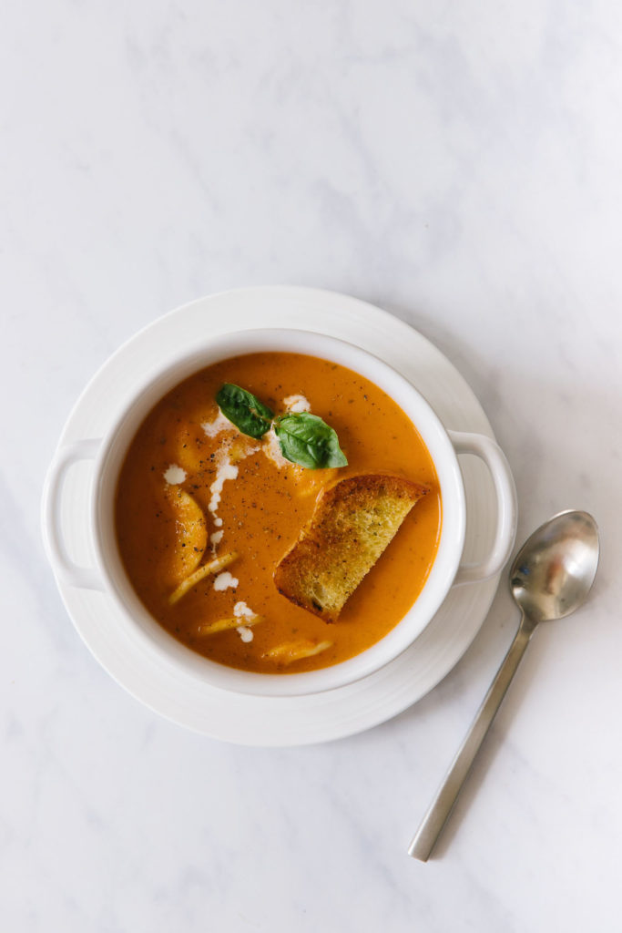white bowl of creamy tomato basil soup garnished with fresh basil and croutons. 