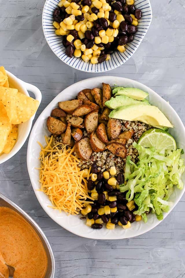 Quinoa burrito bowls with chicken sausage, avocado slices, lime, lettuce, cheese and black beans with corn. 