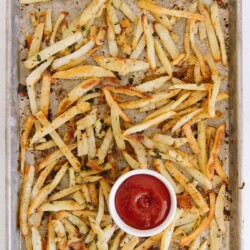 Basil French fries on a baking sheet with a bowl of ketchup.