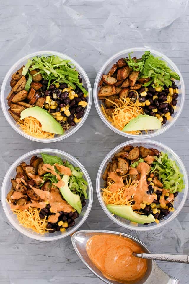 Four make ahead meal prep quinoa burrito bowls filled with Quinoa ,chicken sausage, avocado slices, lime, lettuce, cheese and black beans with corn. 