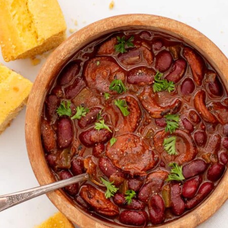 Spoon in a wooden bowl of chili with smoked sausage.