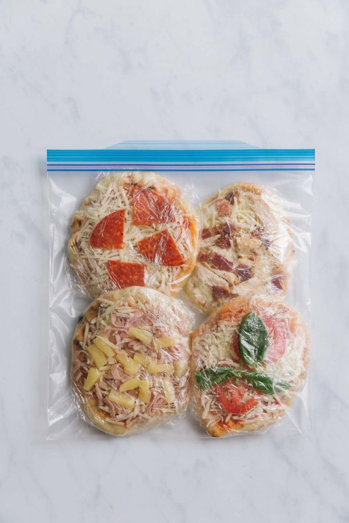 Mini pizzas wrapped in plastic wrap then added to freezer bag. Shows tip to preventing freezer burn