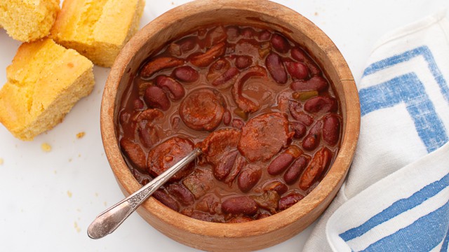 Simple chili with smoked sausage and red kidney beans in wooden bowl and a few squares of cornbread  