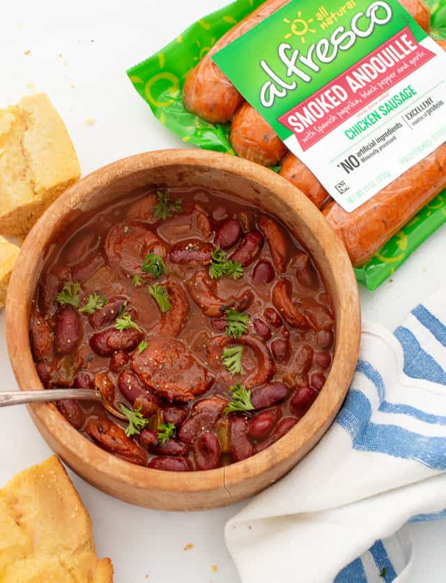 Simple chili with smoked sausage and red kidney beans in wooden bowl and a few squares of cornbread  and al fresco smoked andouille sausage package in background