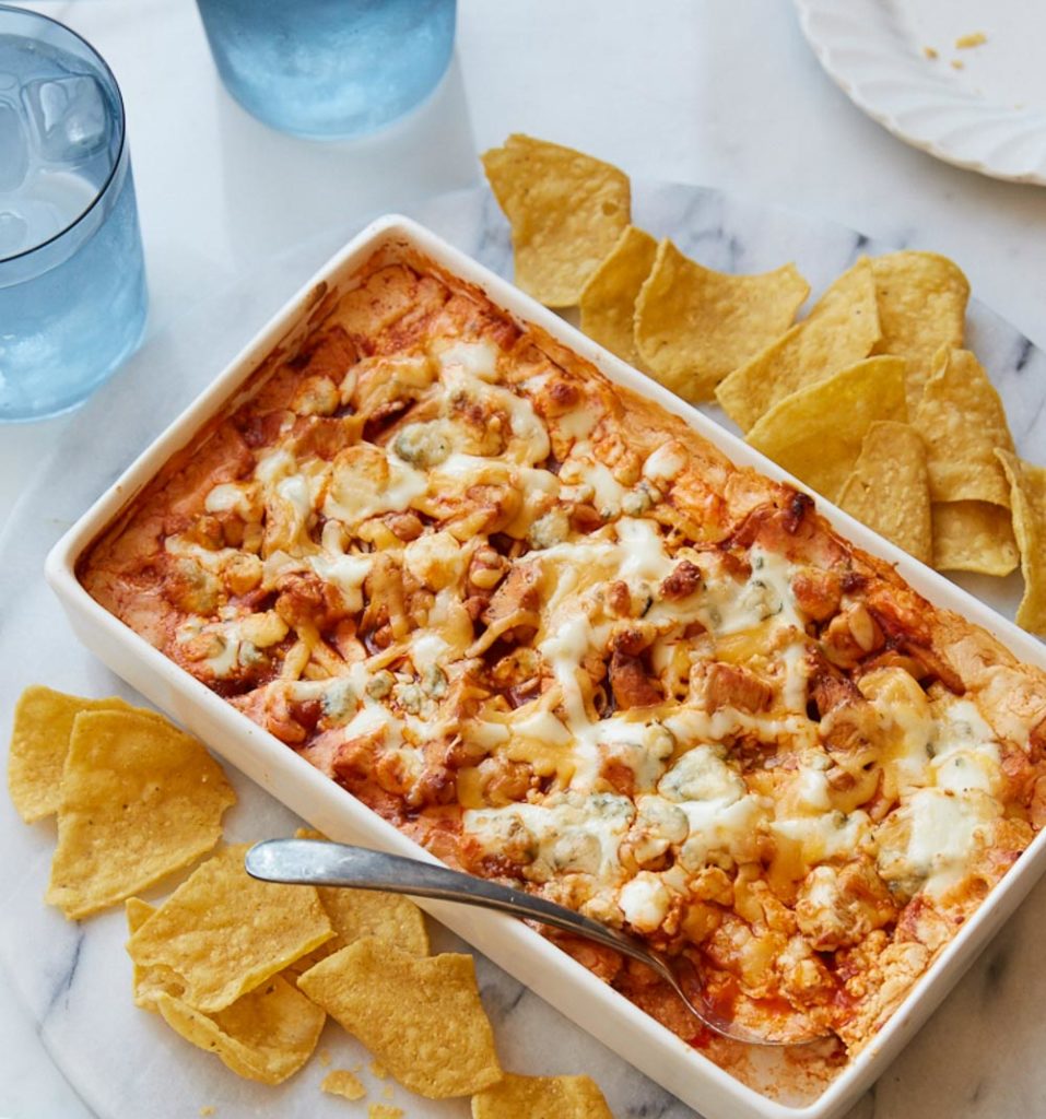 Dip in a white baking dish surrounded by chips and a blue glass in the corner of the pic