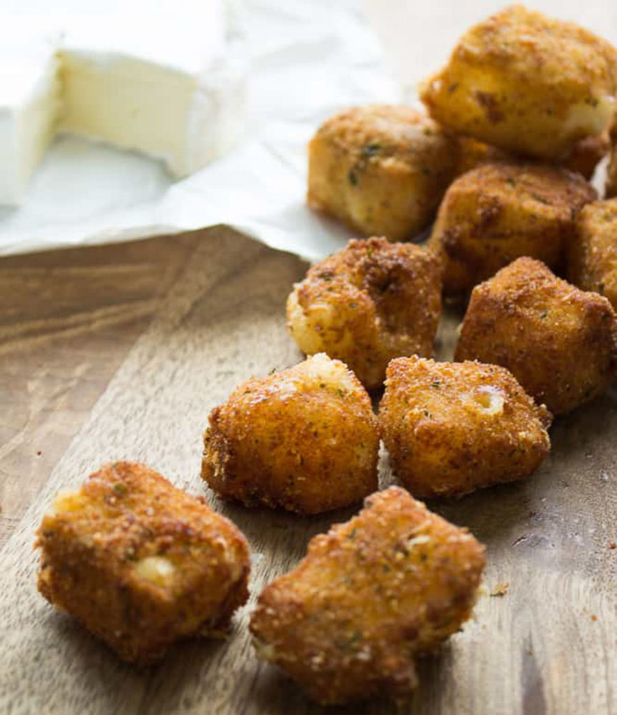 brown balls of fried brie bites with a rind of brie cheese in background on a wooden table