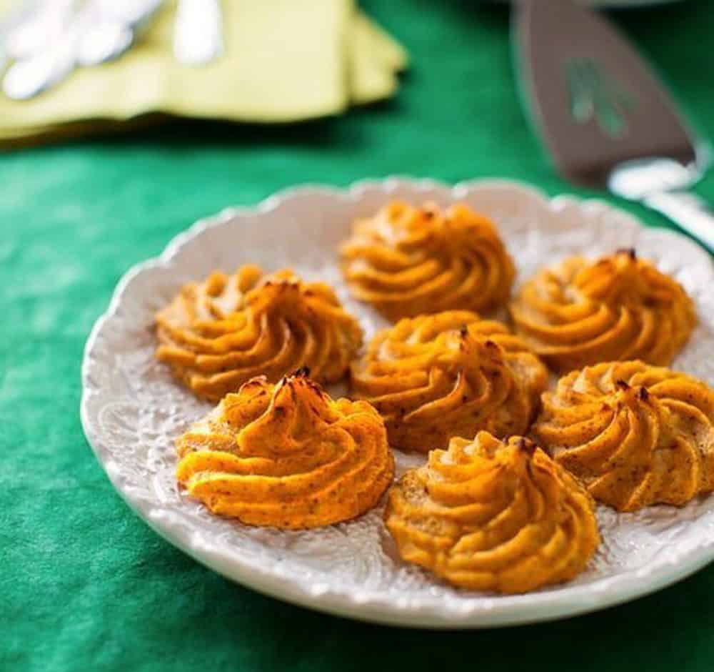 Butternut swirl shaped potato puffs on a plate with a green background. 