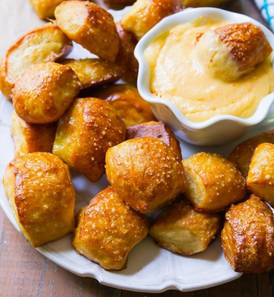 pretzels balls on a white plate with a bowl of cheese sauce with it. 