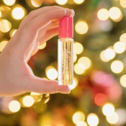 Person holding a container of merry and bright holiday roll-on perfume in from of Christmas lights.