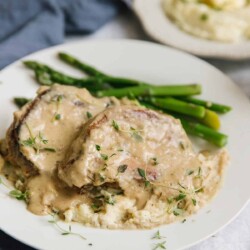 Smothered pot chops on a plate with asparagus.