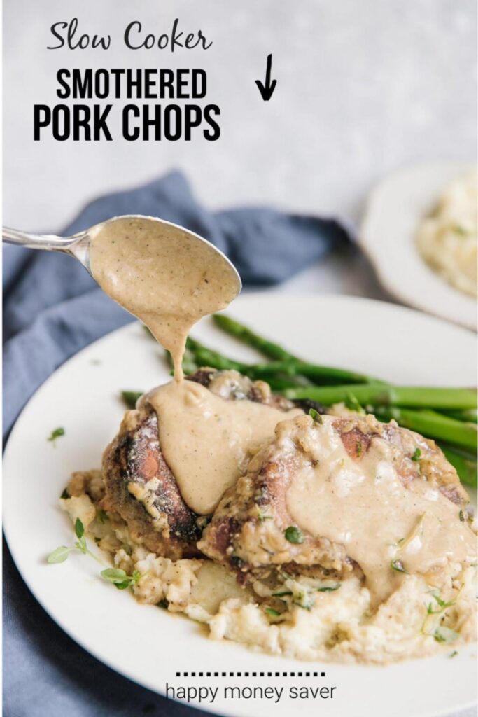 Slow Cooker Smothered Pork Chops recipe. Spooning sauce over pork chops on a white plate with asparagus as a side. 