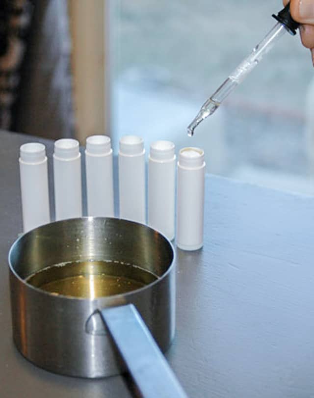 Using a dropper to make homemade lip balm recipe by adding it into tubes. 