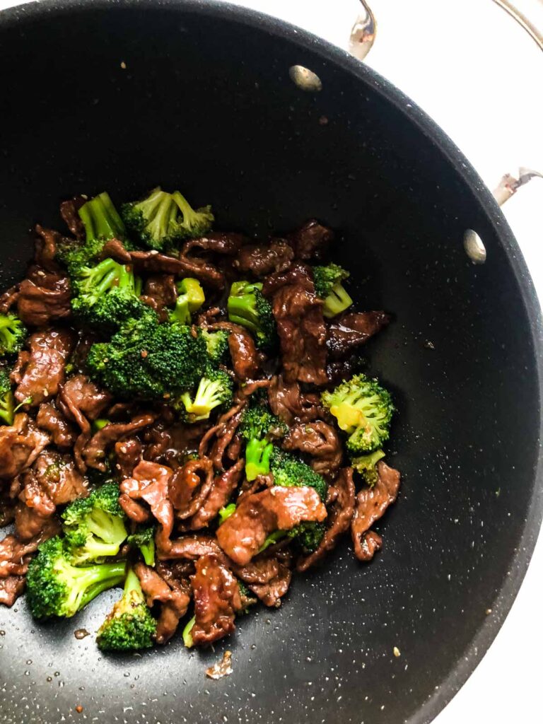 Strips of beef and broccoli cooked altogether smothered in a nonstick pan with a handle.