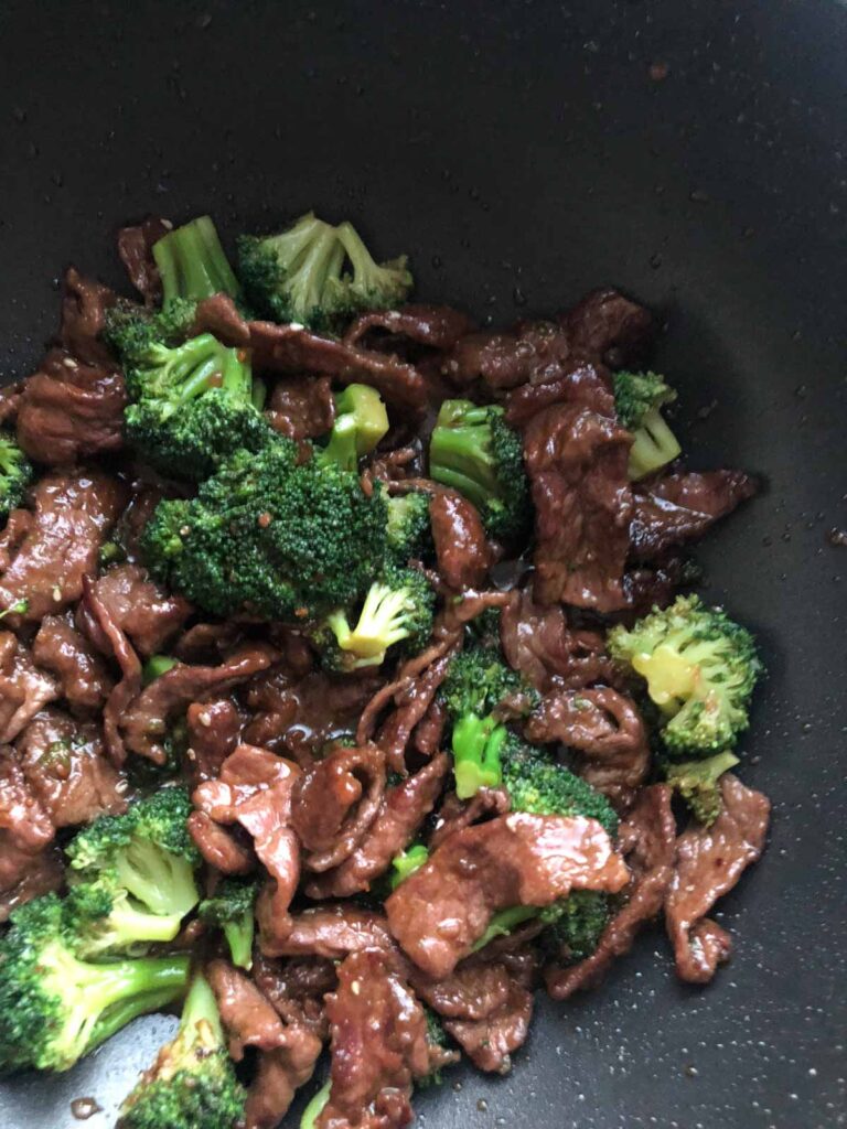 Strips of beef and broccoli cooked altogether smothered in teriyaki sauce in a pan.