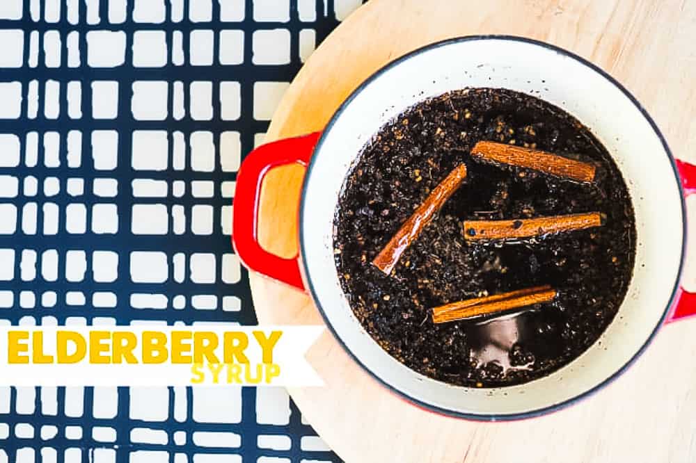 Elderberry syrup recipe cooked in a red handled pot with cinnamon sticks on top.