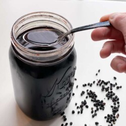 Person using a spoon to scoop elderberry syrup from a glass jar.
