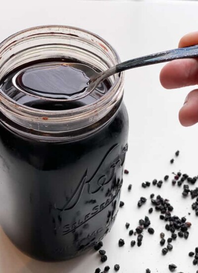 Person using a spoon to scoop elderberry syrup from a glass jar.