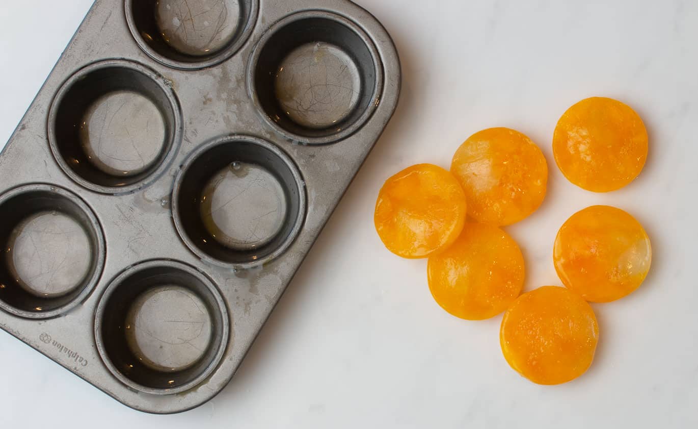 Freezing Eggs to use later can save you money - An empty muffin tin and on the side 6 frozen eggs sitting on a white counter.