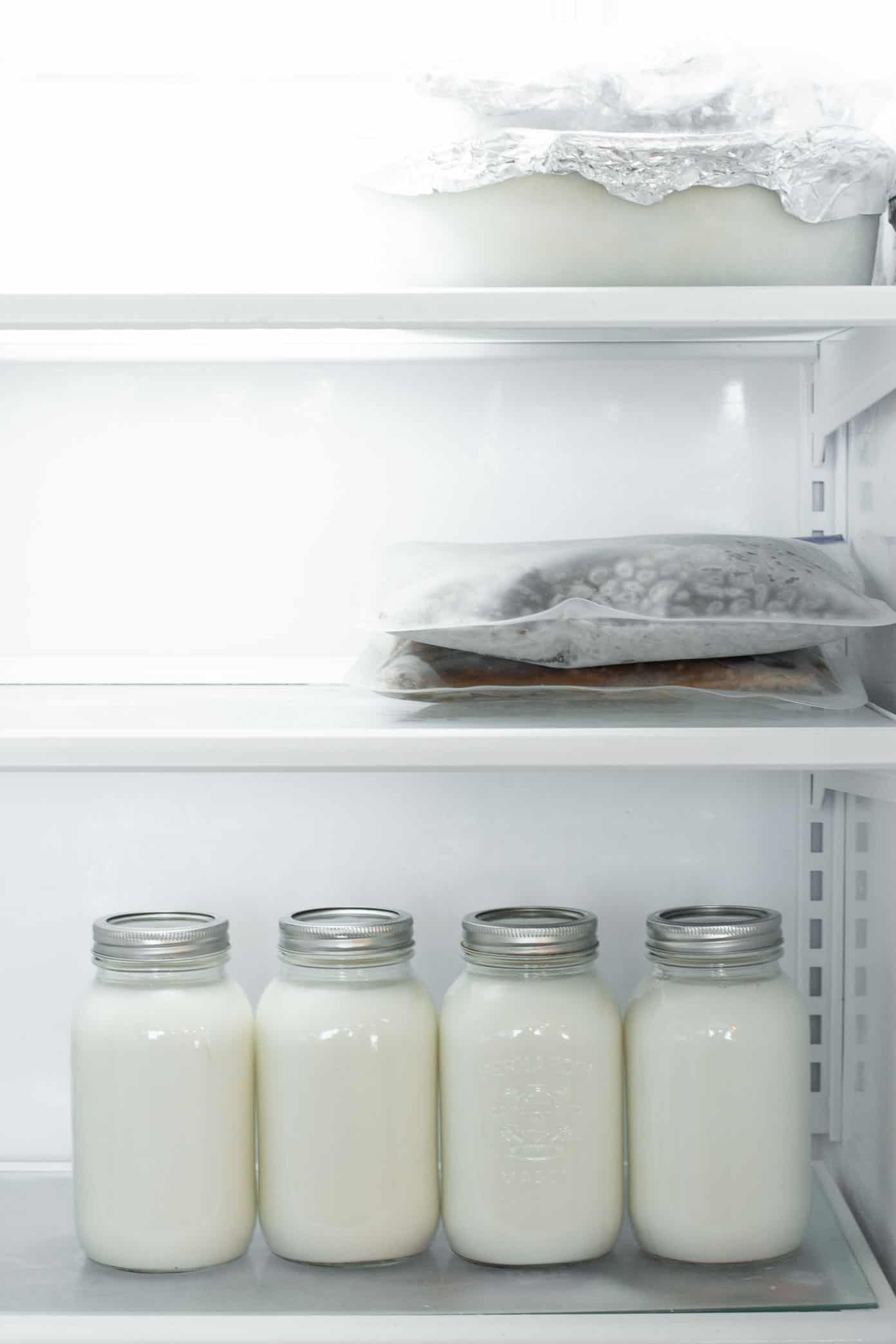 A freezer with three separate shelves. The top shelf has two casserole dishes with foil on them, the middle shelf has two filled resealable bags and the bottom shelf has 4 large mason jars filled with milk.