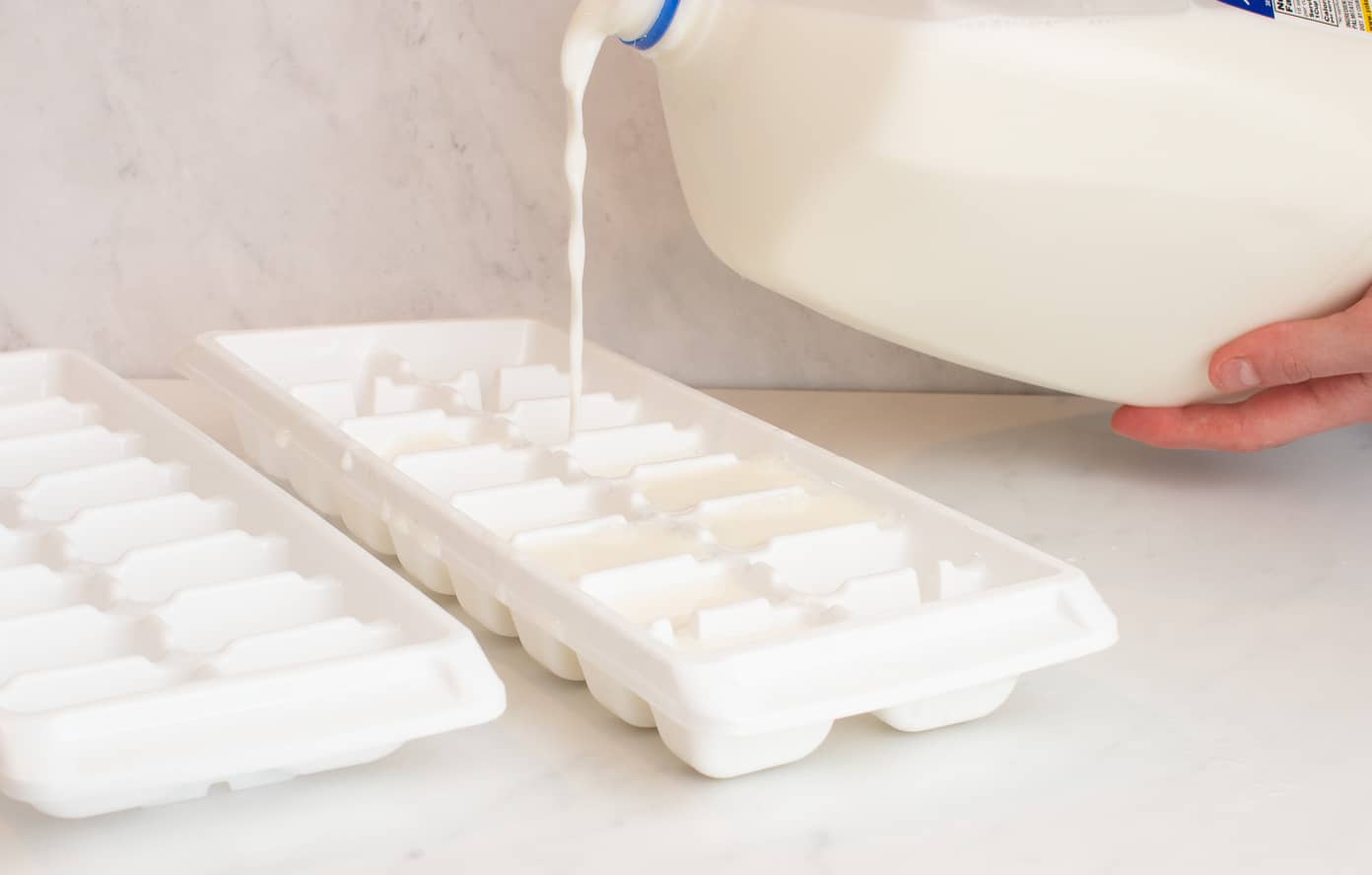 Milk pouring into a white ice cube tray.