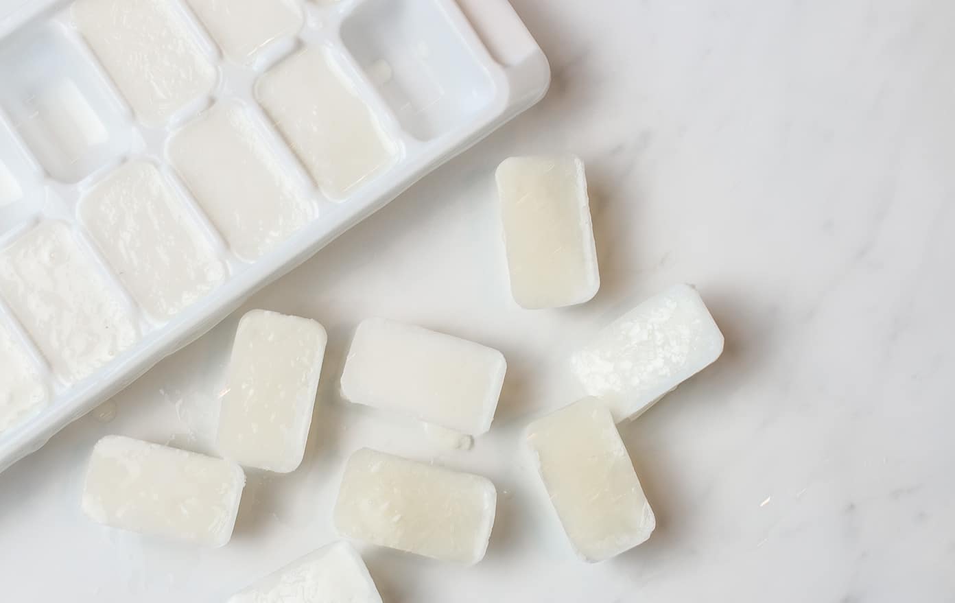 An ice cube tray with milk frozen in cubes at a diagonal on a white counter with 8 cubes sitting on the counter next to it.