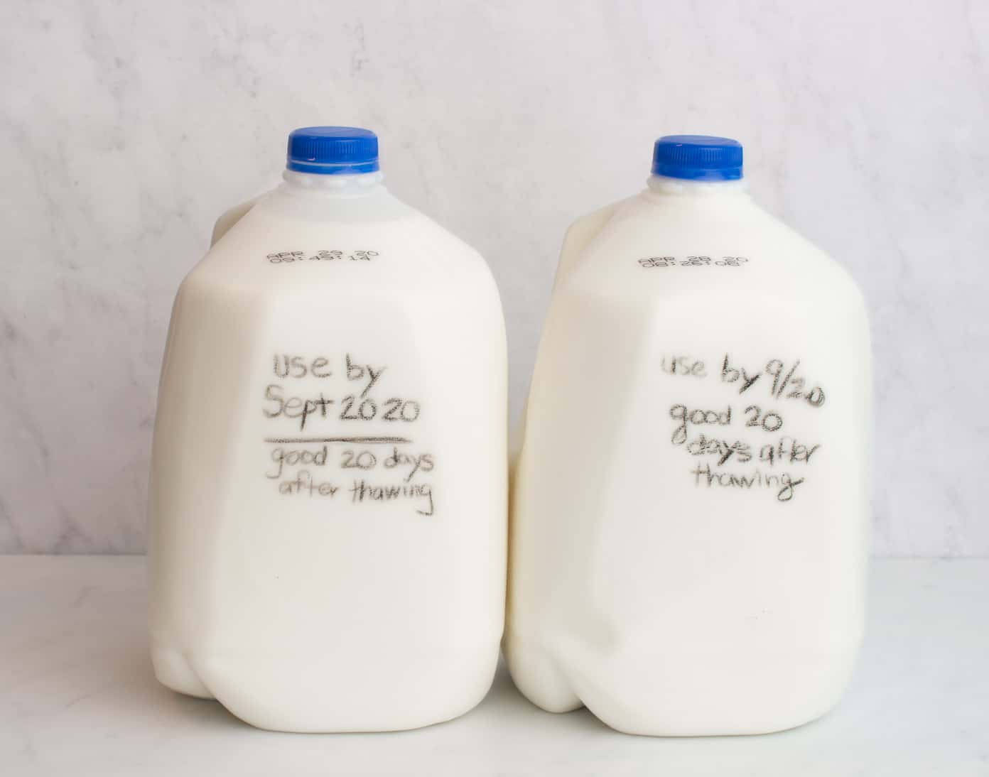 Two gallons of milk on a white counter. The first gallon of milk has the words written on it "use by  Sept 2020." Good for 20 days after thawing. The second has the words "use by 9/20 good for 20 days after thawing" written on it.
