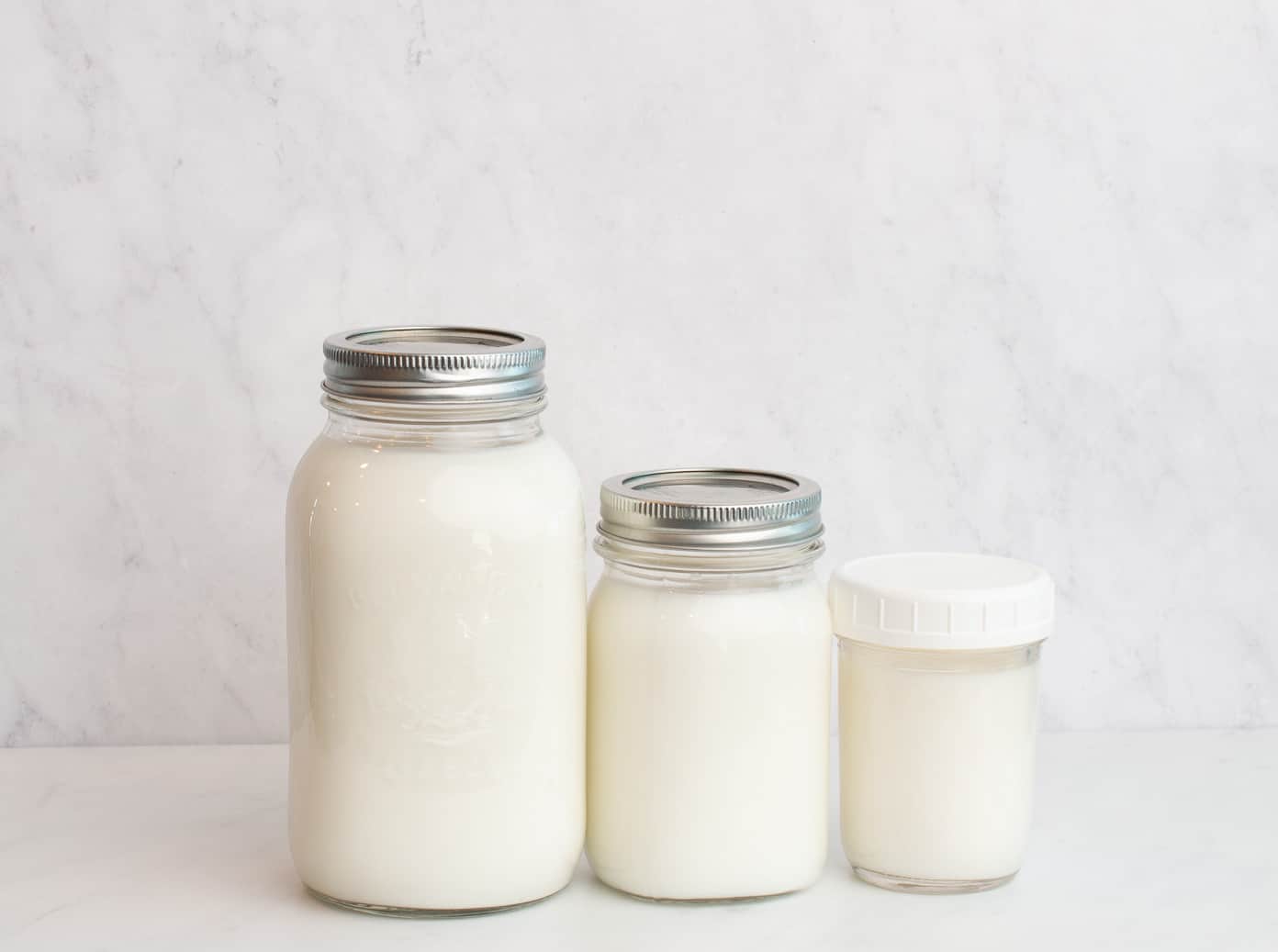 3 mason jars in various sizes lined up on a white counter and a marble background.