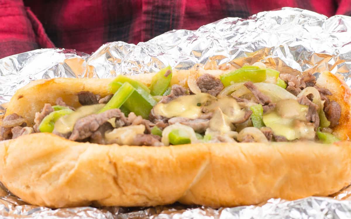 A wooden cutting board holds two Philly cheesesteak sandwiches. This is from a list of make ahead camping meals.
