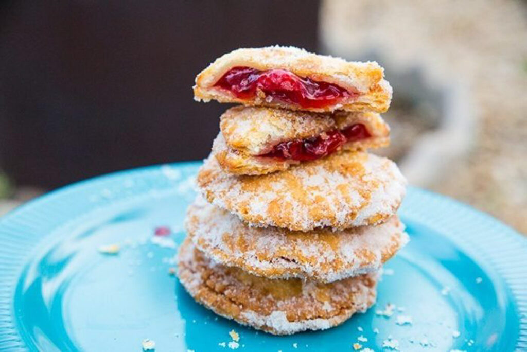 3 whole hand pies on top of each other on a blue plate with one cherry pie split in half on the top of the stack.