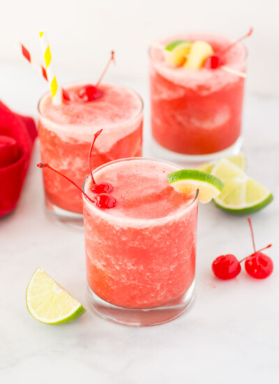 Glasses of pink frozen party stush with fruit toppings.