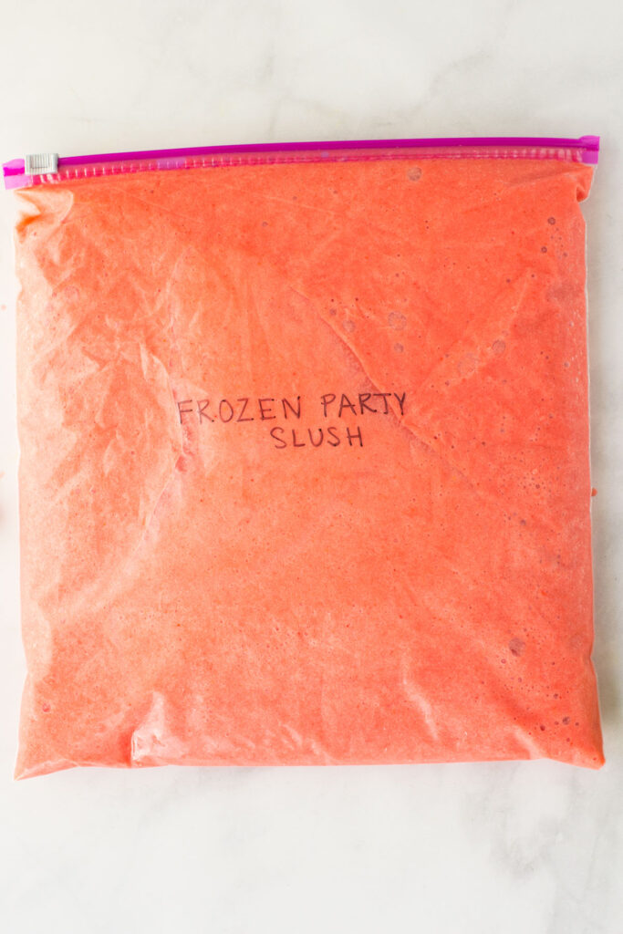 This is a resealable bag filled with a fruit slush recipe with the words "Frozen Party Slush" written on it in black.