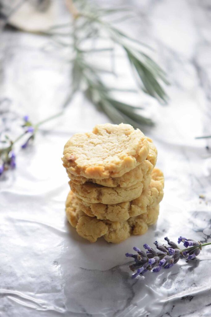 5 lavender cookies stacked on top of each other on a white and black marble counter with sprigs of lavender next to it. 