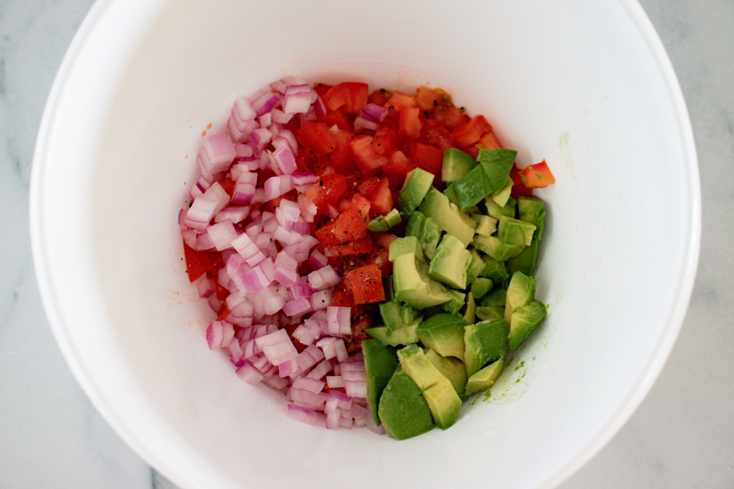 A white bowl of sliced onion, tomato, and avocados.