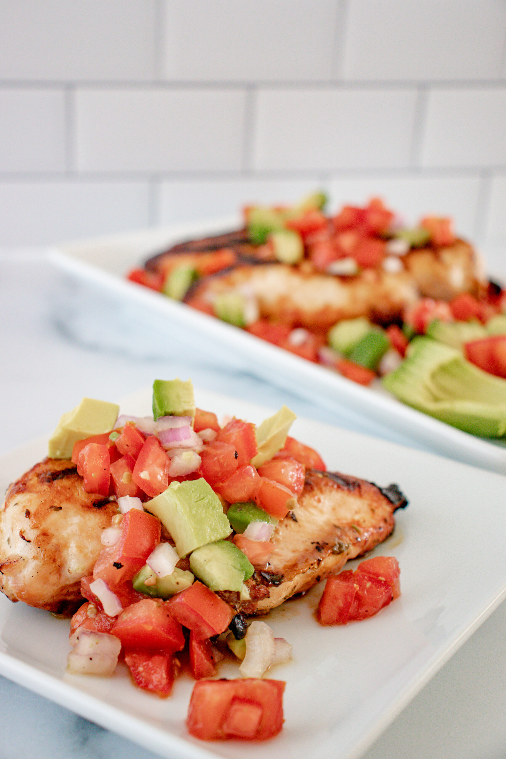 2 white dishes of chicken with avocado salsa.