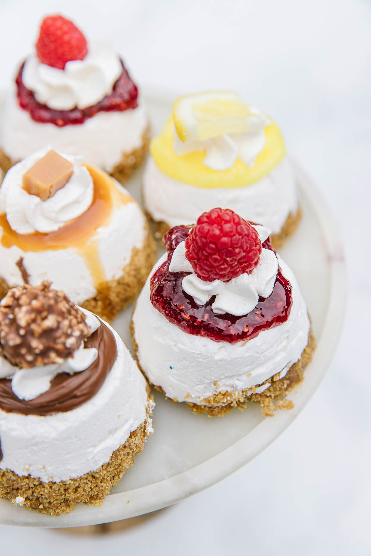 A white dish with 5 mini cheesecakes with different toppings.